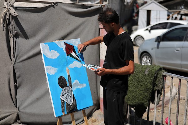 الفنان التشكيلي أحمد الحلبي يرسم طفلًا يمسك بخيط طائرة ورقية تحمل ألوان العلم الفلسطيني، أمام خيمة للنازحين في مدينة غزة،  25 أغسطس/آب 2026.  آخر.( تصوير: بلال أسامة )