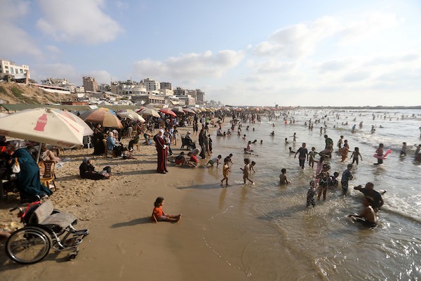 عائلات فلسطينية تقضي وقتاً على شاطئ مدينة غزة هرباً من حرارة الصيف، بينما تصطف خيام النازحين بمحاذاة الساحل، في مشهد يجمع بين البحث عن لحظة راحة وثقل النزوح والحرب، 8 أغسطس/آب 2026. (تصوير: بلال أسامة)