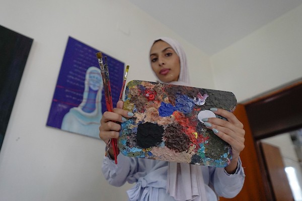 الفنانة نورة القصاص ترسم داخل غرفة بسيطة حولتها إلى مرسم في منزل أحد أقاربها بحي الشيخ رضوان في مدينة غزة، في 12 أغسطس/آب 2026. (تصوير: محمد أبو القمصان)