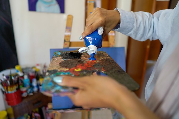 الفنانة نورة القصاص ترسم داخل غرفة بسيطة حولتها إلى مرسم في منزل أحد أقاربها بحي الشيخ رضوان في مدينة غزة، في 12 أغسطس/آب 2026. (تصوير: محمد أبو القمصان)