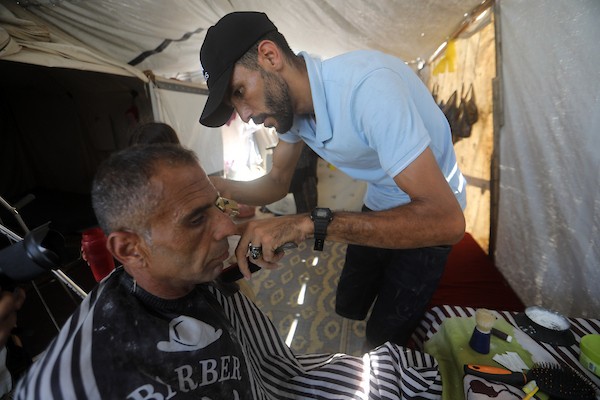 الحلاق الفلسطيني شادي البراوي، 35 عاما، يعمل داخل خيمة نزح إليها مع عائلته في مدينة غزة، في 27 آب/أغسطس 2026، بعدما فقد ساقه اليمنى إثر إصابته بشظايا خلال هجوم إسرائيلي.(تصوير: بلال أسامة)