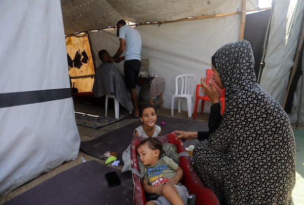 الحلاق الفلسطيني شادي البراوي، 35 عاما، يعمل داخل خيمة نزح إليها مع عائلته في مدينة غزة، في 27 آب/أغسطس 2026، بعدما فقد ساقه اليمنى إثر إصابته بشظايا خلال هجوم إسرائيلي.(تصوير: بلال أسامة)