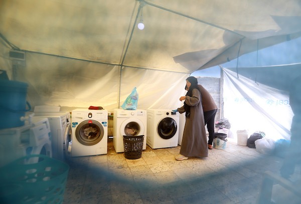 فلسطينيون يغسلون ملابسهم باستخدام غسالات كهربائية داخل مخيم للنازحين غرب مدينة غزة، في 27 أغسطس/آب 2026، وسط صعوبات في تأمين المياه والكهرباء. (تصوير: بلال أسامة)