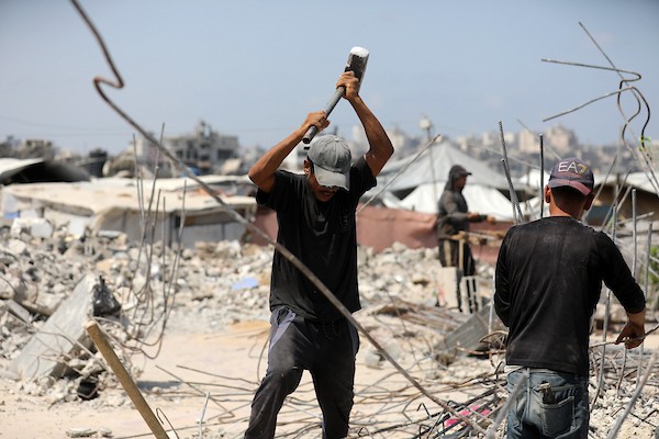 عمال فلسطينيون يستخرجون الحديد من أنقاض منازل مدمرة في حي التفاح بمدينة غزة لإعادة استخدامه في تدعيم خيام ومساكن مؤقتة للنازحين. (تصوير: بلال أسامة)