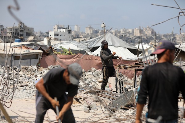 عمال فلسطينيون يستخرجون الحديد من أنقاض منازل مدمرة في حي التفاح بمدينة غزة لإعادة استخدامه في تدعيم خيام ومساكن مؤقتة للنازحين. (تصوير: بلال أسامة)