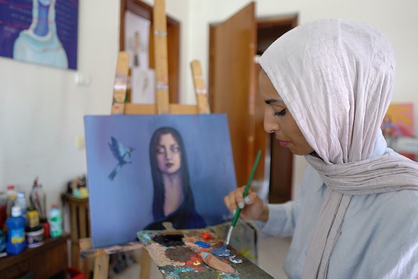 الفنانة نورة القصاص ترسم داخل غرفة بسيطة حولتها إلى مرسم في منزل أحد أقاربها بحي الشيخ رضوان في مدينة غزة، في 12 أغسطس/آب 2026. (تصوير: محمد أبو القمصان)