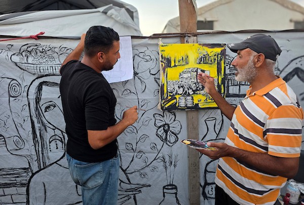 فنانون تشكيليون فلسطينيون يرسمون مشاهد تجسد الغارات والجوع ومعاناة السكان على جدران خيمة للنازحين في منطقة المواصي بخان يونس، جنوب قطاع غزة، في 9 أغسطس/آب 2026، محولين الخيمة إلى سجل بصري يوثق الحياة اليومية في ظل الحرب والنزوح. (تصوير: طارق محمد)