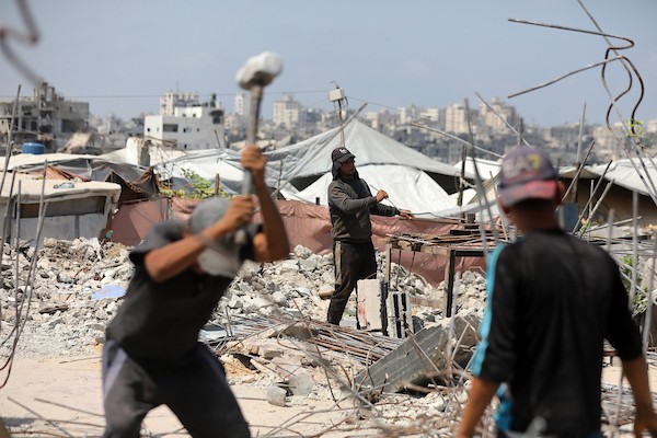 عمال فلسطينيون يستخرجون الحديد من أنقاض منازل مدمرة في حي التفاح بمدينة غزة لإعادة استخدامه في تدعيم خيام ومساكن مؤقتة للنازحين. (تصوير: بلال أسامة)