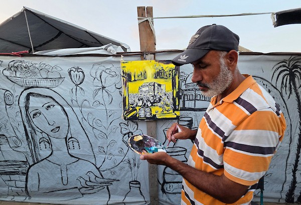 فنانون تشكيليون فلسطينيون يرسمون مشاهد تجسد الغارات والجوع ومعاناة السكان على جدران خيمة للنازحين في منطقة المواصي بخان يونس، جنوب قطاع غزة، في 9 أغسطس/آب 2026، محولين الخيمة إلى سجل بصري يوثق الحياة اليومية في ظل الحرب والنزوح. (تصوير: طارق محمد)