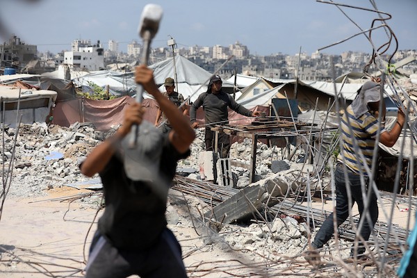 عمال فلسطينيون يستخرجون الحديد من أنقاض منازل مدمرة في حي التفاح بمدينة غزة لإعادة استخدامه في تدعيم خيام ومساكن مؤقتة للنازحين. (تصوير: بلال أسامة)