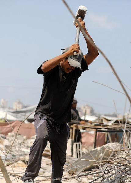 عمال فلسطينيون يستخرجون الحديد من أنقاض منازل مدمرة في حي التفاح بمدينة غزة لإعادة استخدامه في تدعيم خيام ومساكن مؤقتة للنازحين. (تصوير: بلال أسامة)