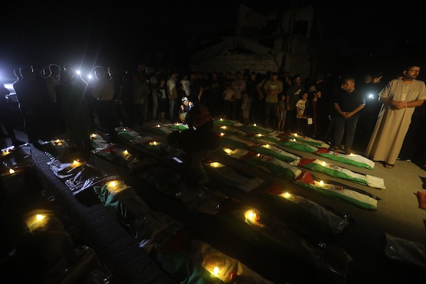 فلسطينيون يتجمعون حول رفات 106 ضحايا غُطيت بالأعلام الفلسطينية وأضيئت إلى جانبها الشموع، خلال مراسم وداع في حي الزيتون بمدينة غزة، 5 أيلول/سبتمبر 2026. تصوير: بلال أسامة