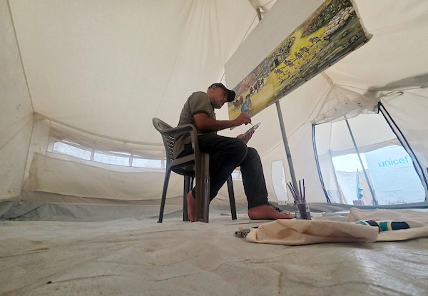الفنان الفلسطيني جهاد الشرافي يرسم داخل خيمة للنازحين في خان يونس جنوبي قطاع غزة، مشاهد توثق الحرب والجوع ونقص المياه والدمار، في 18 سبتمبر/أيلول 2026. تصوير: طارق محمد
