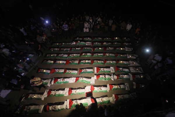 فلسطينيون يتجمعون حول رفات 106 ضحايا غُطيت بالأعلام الفلسطينية وأضيئت إلى جانبها الشموع، خلال مراسم وداع في حي الزيتون بمدينة غزة، 5 أيلول/سبتمبر 2026. تصوير: بلال أسامة