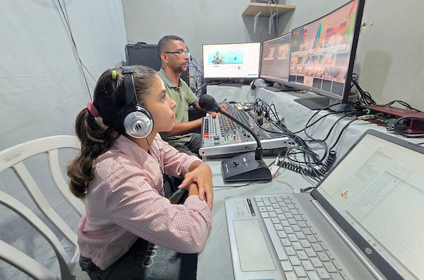 أطفال فلسطينيون يشاركون في إعداد وتقديم برامج لقناة طلائع فلسطين من استوديو متواضع أُقيم داخل خيام النزوح في منطقة مواصي خان يونس. (تصوير: طارق محمد)