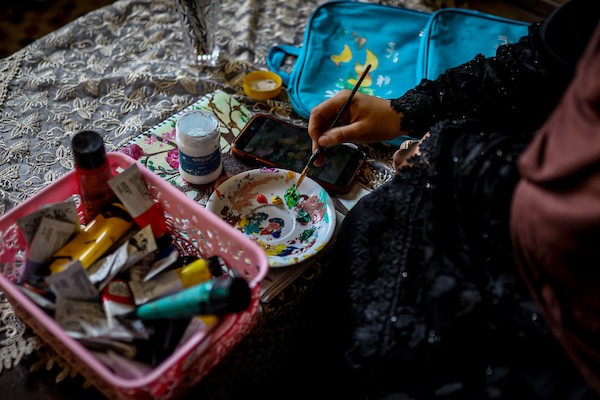 الفنانة التشكيلية هالة أبو حمدة، 18 عامًا، ترسم وتلوّن حقائب مدرسية للأطفال داخل منزلها في حي النصر بمدينة غزة، في 27 سبتمبر/أيلول 2026. صورة: بلال أسامة