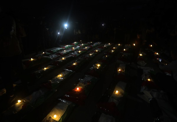 فلسطينيون يتجمعون حول رفات 106 ضحايا غُطيت بالأعلام الفلسطينية وأضيئت إلى جانبها الشموع، خلال مراسم وداع في حي الزيتون بمدينة غزة، 5 أيلول/سبتمبر 2026. تصوير: بلال أسامة