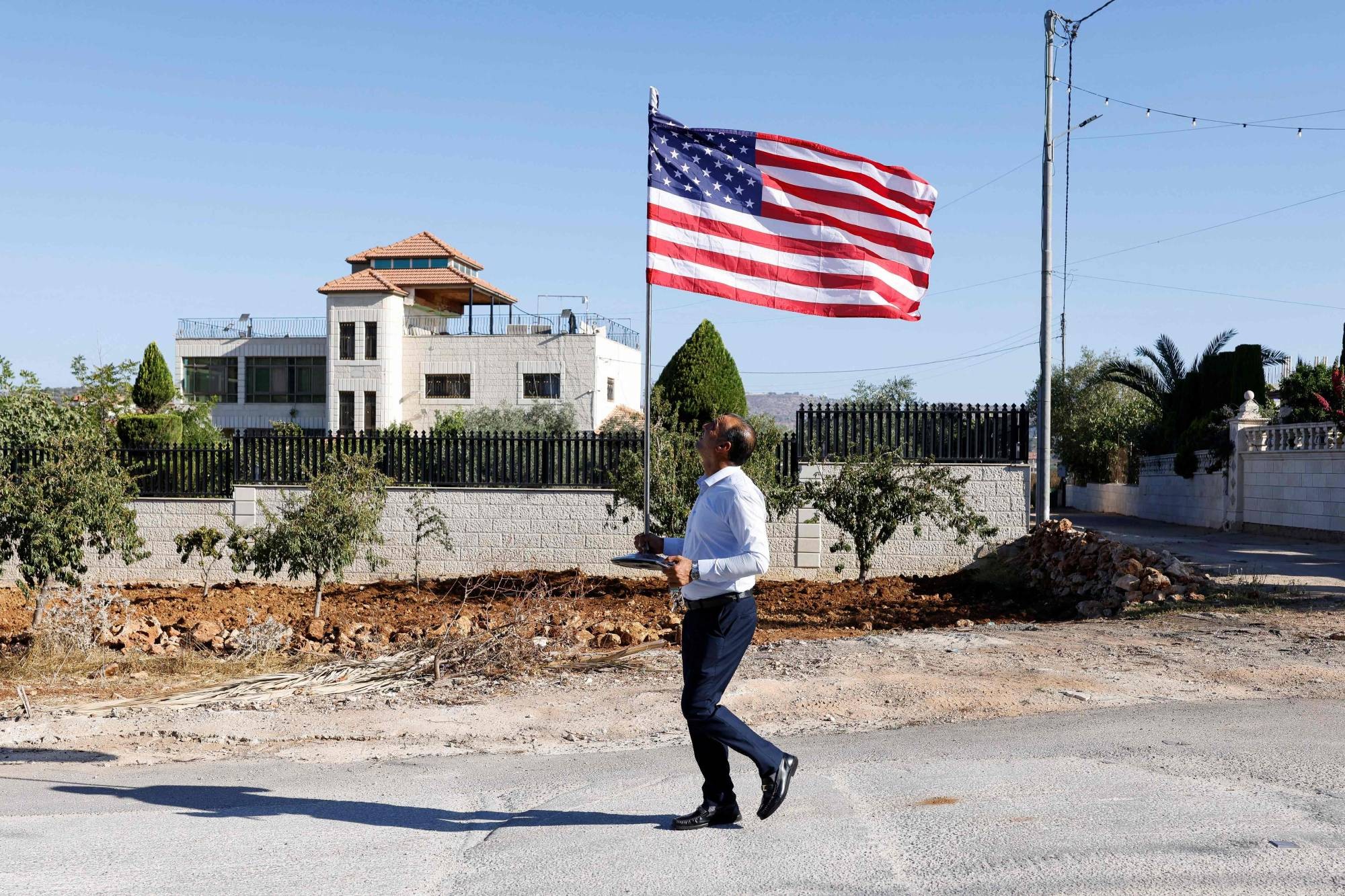 فلسطيني يحمل الجنسية الأميركية يسير حاملاً علماً أميركياً خلال زيارة السفير الأميركي لدى إسرائيل مايك هاكابي بلدة ترمسعيَّا قرب رام الله في الضفة الغربية (أ.ف.ب).jpeg