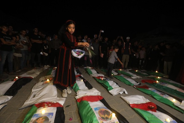 فلسطينيون يتجمعون حول رفات 106 ضحايا غُطيت بالأعلام الفلسطينية وأضيئت إلى جانبها الشموع، خلال مراسم وداع في حي الزيتون بمدينة غزة، 5 أيلول/سبتمبر 2026. تصوير: بلال أسامة