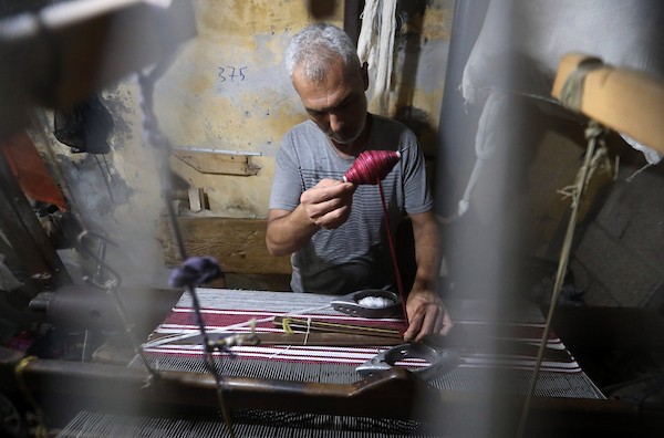 عمال فلسطينيون يصنعون السجاد يدويًا باستخدام أدوات بسيطة داخل متجر شرقي مدينة غزة، في 31 آب/أغسطس 2026. (تصوير: بلال أسامة)