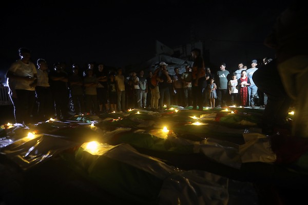 فلسطينيون يتجمعون حول رفات 106 ضحايا غُطيت بالأعلام الفلسطينية وأضيئت إلى جانبها الشموع، خلال مراسم وداع في حي الزيتون بمدينة غزة، 5 أيلول/سبتمبر 2026. تصوير: بلال أسامة