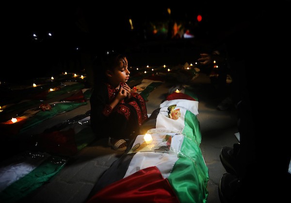 فلسطينيون يتجمعون حول رفات 106 ضحايا غُطيت بالأعلام الفلسطينية وأضيئت إلى جانبها الشموع، خلال مراسم وداع في حي الزيتون بمدينة غزة، 5 أيلول/سبتمبر 2026. تصوير: بلال أسامة