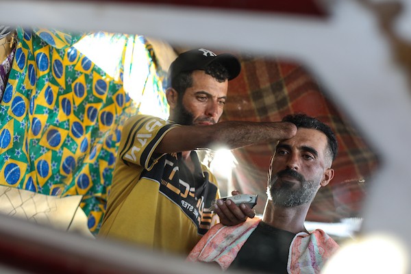 الحلاق جهاد المبحوح (38 عاماً) يواصل عمله داخل خيمة في مخيم النصيرات وسط قطاع غزة، في 20 سبتمبر/أيلول 2026، بعد فقدانه إحدى يديه إثر إصابته في غارة إسرائيلية. (صورة: حسن الجدي)