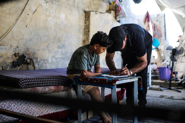 الطفل الفلسطيني كنان أبو جبة، الناجي الوحيد من عائلته بعد استهداف منزلهم في حي الشجاعية، يكتب في دفتره داخل خيمة بمدينة غزة مستخدمًا طرفًا صناعيًا بعد بتر يده اليسرى، 21 سبتمبر/أيلول 2026. تصوير: بلال أسامة.