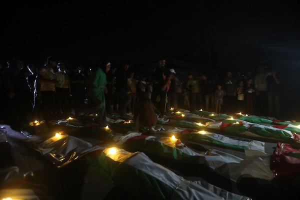 فلسطينيون يتجمعون حول رفات 106 ضحايا غُطيت بالأعلام الفلسطينية وأضيئت إلى جانبها الشموع، خلال مراسم وداع في حي الزيتون بمدينة غزة، 5 أيلول/سبتمبر 2026. تصوير: بلال أسامة