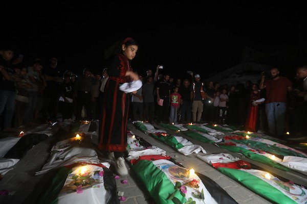 فلسطينيون يتجمعون حول رفات 106 ضحايا غُطيت بالأعلام الفلسطينية وأضيئت إلى جانبها الشموع، خلال مراسم وداع في حي الزيتون بمدينة غزة، 5 أيلول/سبتمبر 2026. تصوير: بلال أسامة