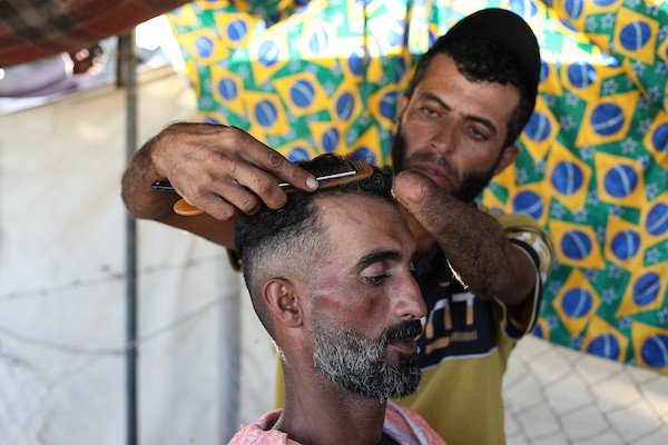 الحلاق جهاد المبحوح (38 عاماً) يواصل عمله داخل خيمة في مخيم النصيرات وسط قطاع غزة، في 20 سبتمبر/أيلول 2026، بعد فقدانه إحدى يديه إثر إصابته في غارة إسرائيلية. (صورة: حسن الجدي)