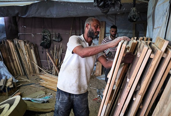 النجار الفلسطيني إياد أبو عامر يصنع مقاعد دراسية من أخشاب انتُشلت من أنقاض المنازل المدمرة وصناديق الإغاثة وقطع المعادن في خان يونس جنوب قطاع غزة، مع انطلاق العام الدراسي الجديد في 21 سبتمبر/أيلول 2026. تصوير: طارق محمد.