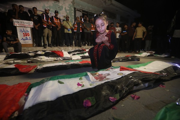 فلسطينيون يتجمعون حول رفات 106 ضحايا غُطيت بالأعلام الفلسطينية وأضيئت إلى جانبها الشموع، خلال مراسم وداع في حي الزيتون بمدينة غزة، 5 أيلول/سبتمبر 2026. تصوير: بلال أسامة