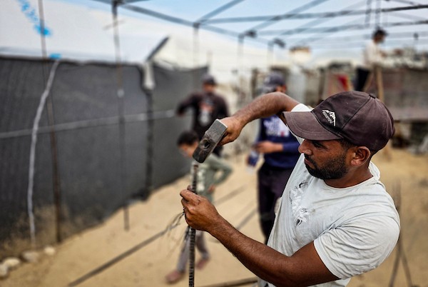 فلسطينيون يستخدمون قضبانًا معدنية انتشلوها من أنقاض منازل مدمرة لإقامة خيام تؤوي عائلات نازحة في منطقة المواصي بخان يونس، في 12 أكتوبر/تشرين الأول 2026، استعدادًا لفصل الشتاء.(تصوير: طارق محمد)