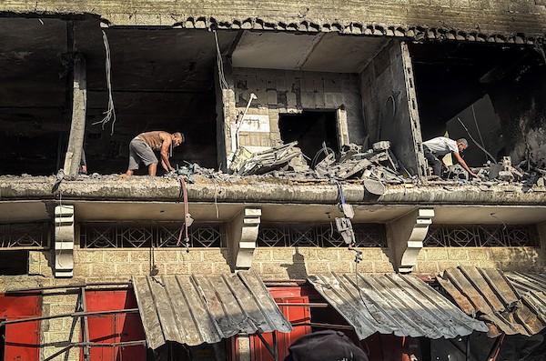 فلسطينيون يتفقدون ما تبقى من ممتلكاتهم وسط أنقاض مبنى سكني استهدفته غارة جوية إسرائيلية في مخيم المغازي للاجئين وسط قطاع غزة، يوم 16 أكتوبر/تشرين الأول 2026. (تصوير: أحمد إبراهيم)