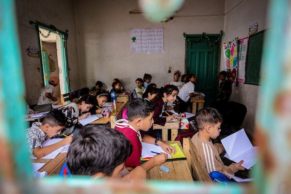 أطفال فلسطينيون يواصلون تعليمهم على مقاعد مصنوعة من صناديق المساعدات المُعاد تدويرها في مدينة غزة، وسط دمار المدارس ونقص المستلزمات التعليمية. (تصوير: محمد صالحة)