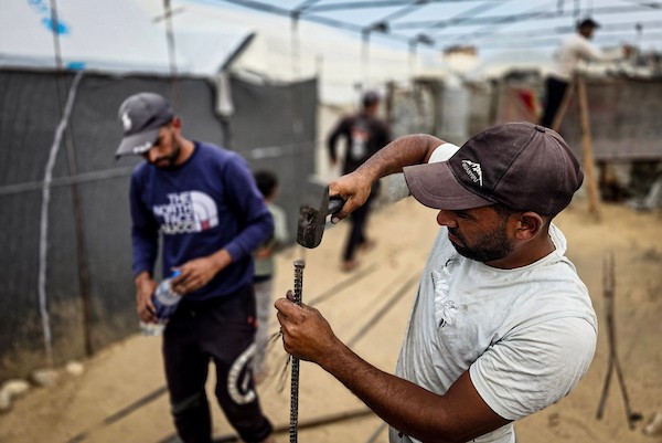 فلسطينيون يستخدمون قضبانًا معدنية انتشلوها من أنقاض منازل مدمرة لإقامة خيام تؤوي عائلات نازحة في منطقة المواصي بخان يونس، في 12 أكتوبر/تشرين الأول 2026، استعدادًا لفصل الشتاء.(تصوير: طارق محمد)
