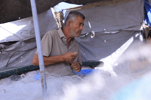 الصياد الفلسطيني محمد التوم (61 عامًا) يصلح بمساعدة أطفاله شباكًا انتشلها من أنقاض منزله المدمر في قطاع غزة.تصوير: عبد الله أبو الخير.