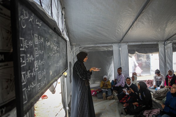 طلاب يتلقون دروسهم جلوسًا على الأرض داخل خيام تفتقر إلى المقاعد والتجهيزات المدرسية في مركز سرايا التعليمي بقطاع غزة، 11 أكتوبر/تشرين الأول 2026. (تصوير: محمد صالحة)
