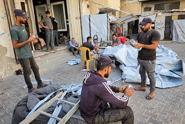 الخياط الفلسطيني شعبان الطباش يصلح أغطية بلاستيكية وقماشًا مشمعًا لتقوية خيام النازحين وحمايتها من برد الشتاء وأمطاره، في خان يونس جنوب قطاع غزة، 4 أكتوبر/تشرين الأول 2026. (تصوير: طارق محمد)