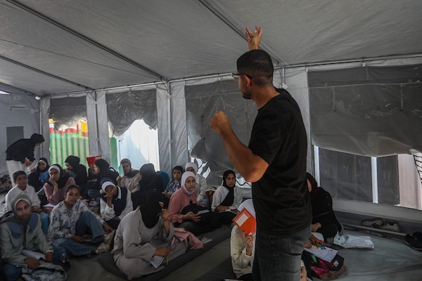 طلاب يتلقون دروسهم جلوسًا على الأرض داخل خيام تفتقر إلى المقاعد والتجهيزات المدرسية في مركز سرايا التعليمي بقطاع غزة، 11 أكتوبر/تشرين الأول 2026. (تصوير: محمد صالحة)