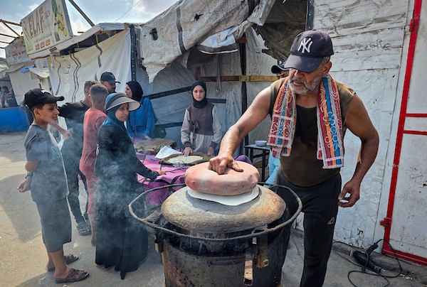 الفلسطيني مازن الدوش يُعدّ الخبز على صاج بدائي بين أنقاض المباني المدمرة في خان يونس، جنوب قطاع غزة، 9 تشرين الأول/أكتوبر 2026. (تصوير: طارق محمد)