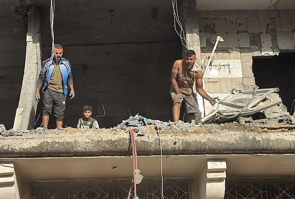 فلسطينيون يتفقدون ما تبقى من ممتلكاتهم وسط أنقاض مبنى سكني استهدفته غارة جوية إسرائيلية في مخيم المغازي للاجئين وسط قطاع غزة، يوم 16 أكتوبر/تشرين الأول 2026. (تصوير: أحمد إبراهيم)