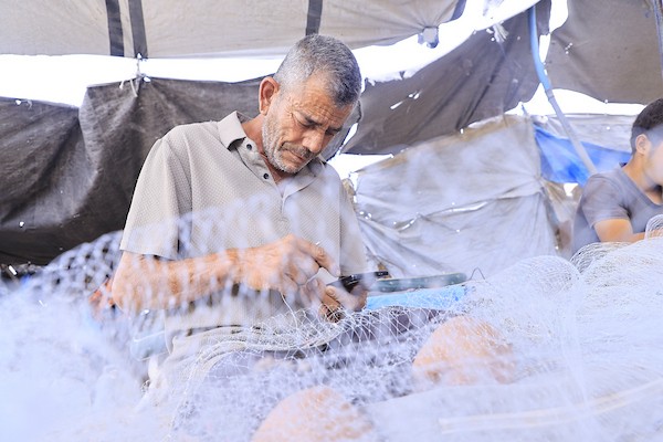 الصياد الفلسطيني محمد التوم (61 عامًا) يصلح بمساعدة أطفاله شباكًا انتشلها من أنقاض منزله المدمر في قطاع غزة.تصوير: عبد الله أبو الخير.