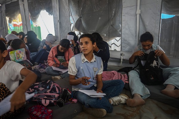 طلاب يتلقون دروسهم جلوسًا على الأرض داخل خيام تفتقر إلى المقاعد والتجهيزات المدرسية في مركز سرايا التعليمي بقطاع غزة، 11 أكتوبر/تشرين الأول 2026. (تصوير: محمد صالحة)