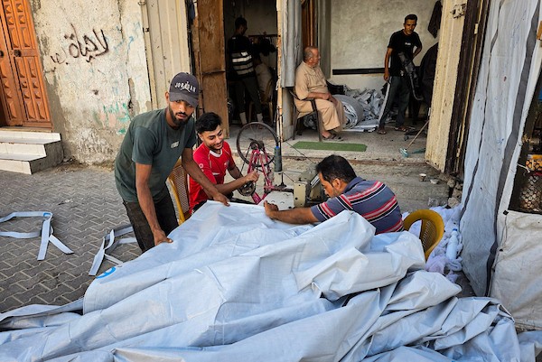 الخياط الفلسطيني شعبان الطباش يصلح أغطية بلاستيكية وقماشًا مشمعًا لتقوية خيام النازحين وحمايتها من برد الشتاء وأمطاره، في خان يونس جنوب قطاع غزة، 4 أكتوبر/تشرين الأول 2026. (تصوير: طارق محمد)