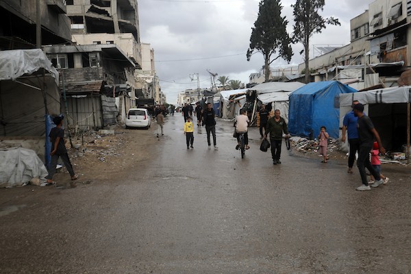 تحت أمطار غزة، يسير فلسطينيون نازحون وسط ظروف معيشية قاسية، فيما يحاول آخرون تغطية خيامهم لمنع تسرب مياه الأمطار إليها، في 18 أكتوبر/تشرين الأول 2026.تصوير: محمد صالحة