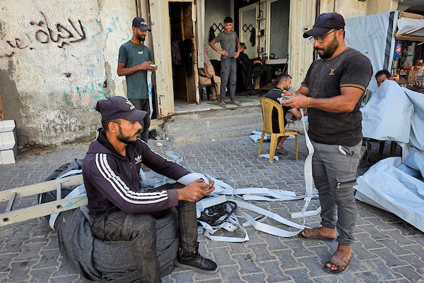 الخياط الفلسطيني شعبان الطباش يصلح أغطية بلاستيكية وقماشًا مشمعًا لتقوية خيام النازحين وحمايتها من برد الشتاء وأمطاره، في خان يونس جنوب قطاع غزة، 4 أكتوبر/تشرين الأول 2026. (تصوير: طارق محمد)