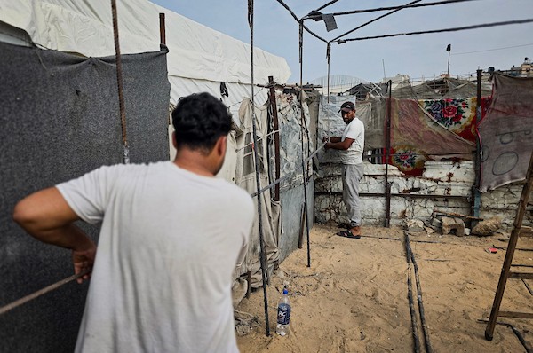 فلسطينيون يستخدمون قضبانًا معدنية انتشلوها من أنقاض منازل مدمرة لإقامة خيام تؤوي عائلات نازحة في منطقة المواصي بخان يونس، في 12 أكتوبر/تشرين الأول 2026، استعدادًا لفصل الشتاء.(تصوير: طارق محمد)