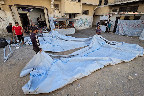 الخياط الفلسطيني شعبان الطباش يصلح أغطية بلاستيكية وقماشًا مشمعًا لتقوية خيام النازحين وحمايتها من برد الشتاء وأمطاره، في خان يونس جنوب قطاع غزة، 4 أكتوبر/تشرين الأول 2026. (تصوير: طارق محمد)